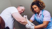 Caregiving nurse putting a bandage on a senior man's arm in his home.